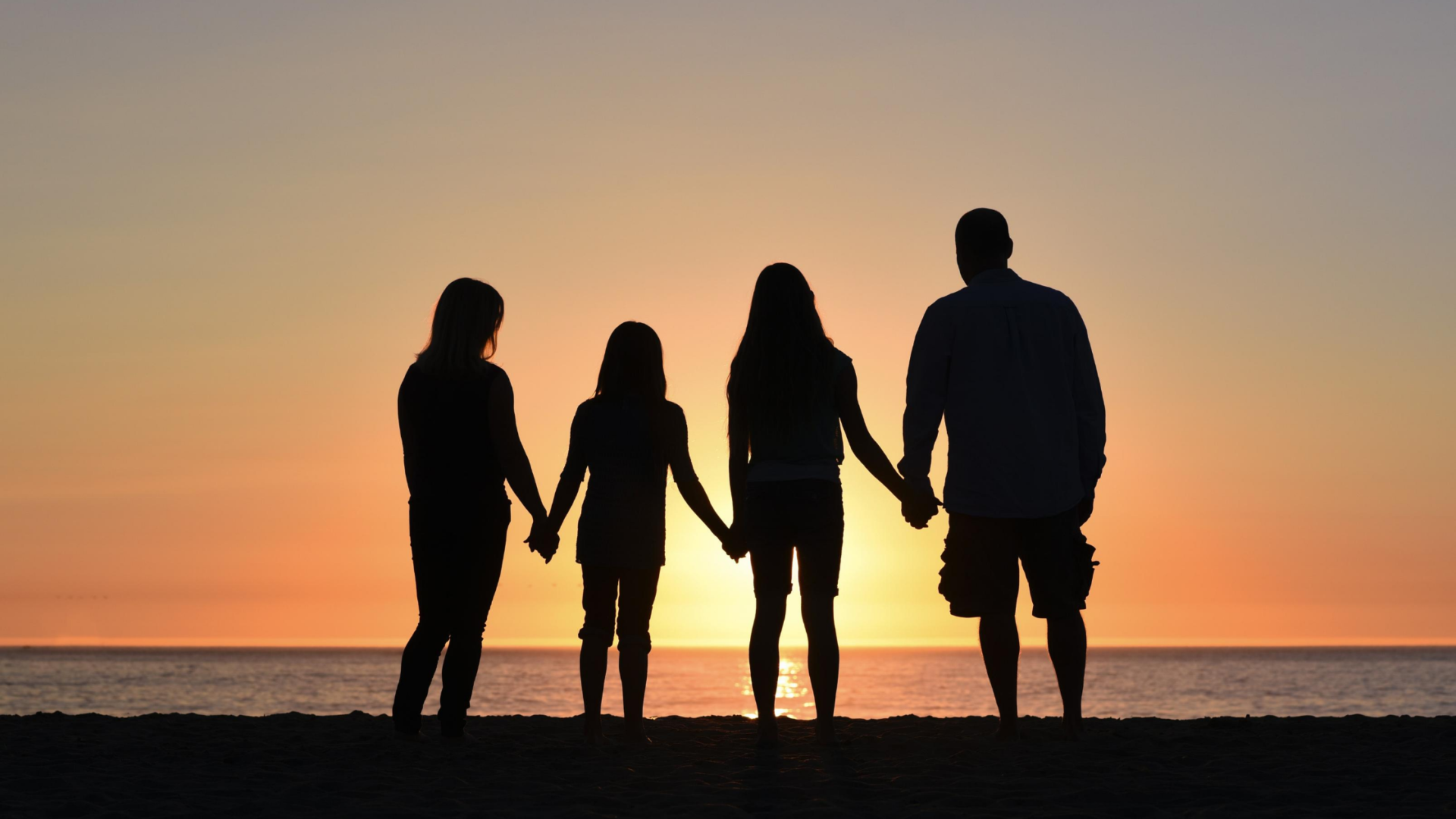 mother, two daughter, and dad holding hands and silhouetted before a sunset